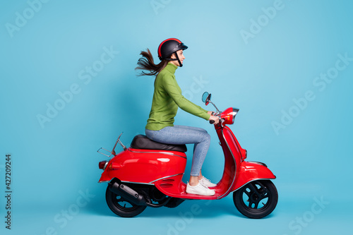 Full length side profile photo portrait of woman in helmet driving red scooter isolated on pastel blue colored background