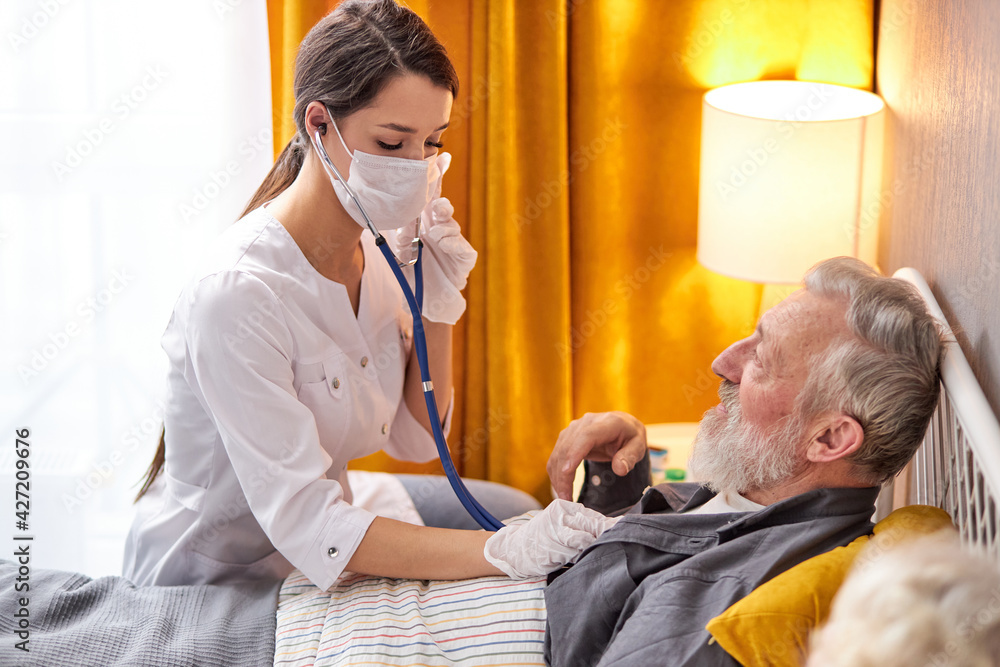 Fototapeta premium Young nurse take care senior man on a bed, nurse listen to sounds in heart or lungs using stethoscope