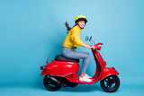 Full length photo portrait of cute girl driving red scooter isolated on pastel blue colored background