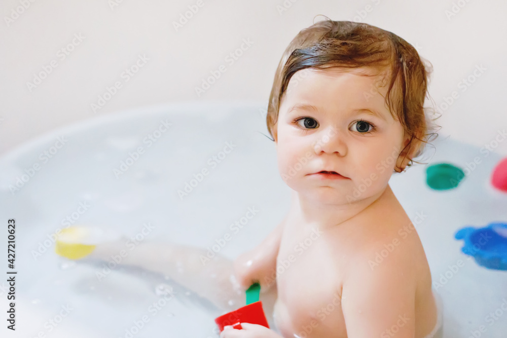 Cute adorable baby girl taking foamy bath in bathtub. Toddler playing with bath rubber toys. Beautiful child having fun with colorful gum toys and foam bubbles. Cute adorable baby girl taking foamy bath in bathtub. Toddler playing with bath rubber toys. Beautiful child having fun with colorful gum toys and foam bubbles.