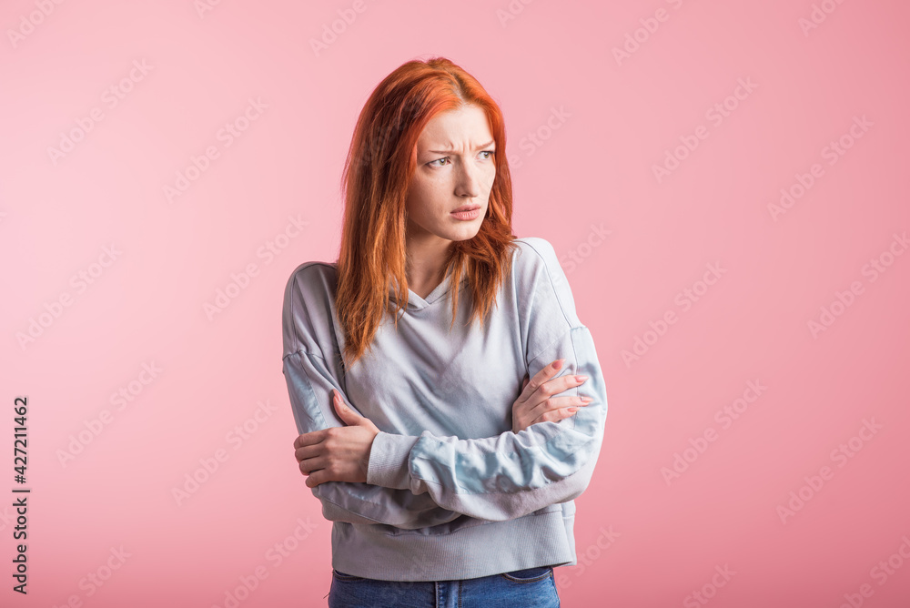 Upset redhead girl with crossed arms in the studio on a pink background Upset redhead girl with crossed arms in the studio on a pink background