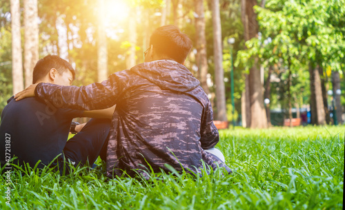 Canvastavla two asian man friends sitting on green grass in the park, encouraging, comfortin
