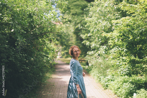 Happy mature woman at the local park Middle aged woman in garden. Healthy lifestyle of maturity people. Rear view of female person in blue vintage dress. Scenic summer photo, copy space