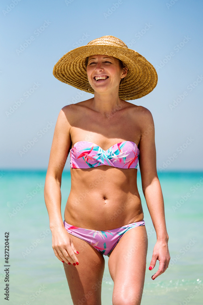 Woman walking out of the sea smiling wearing straw hat
