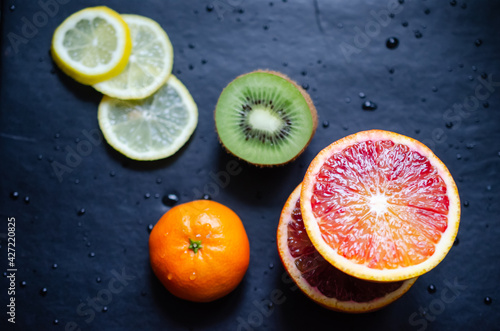 Mix of fresh tropical fruits including blood orange, kiwi, clementine and lemon slices on back worktop covered with water drops. © Valentina Sandu