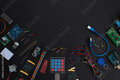 various microcircuits, controllers, sensors, parts, motherboard, cable, wires and a soldering iron on a muted black background.. copy space. flatlay photo