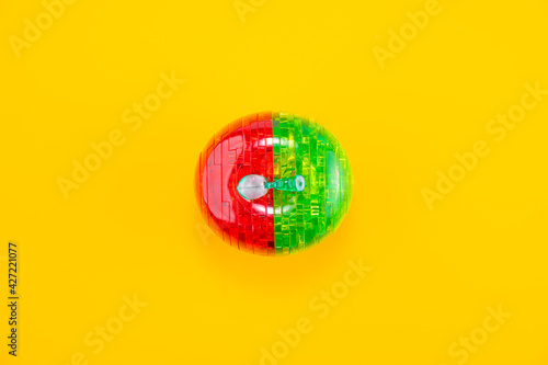 Assembled red-green plastic puzzle in the shape of an apple, on the yellow background.