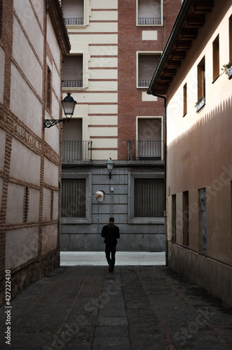 Man walking down a narrow, shady street surrounded by walls leading to a brighter one © Jonathan