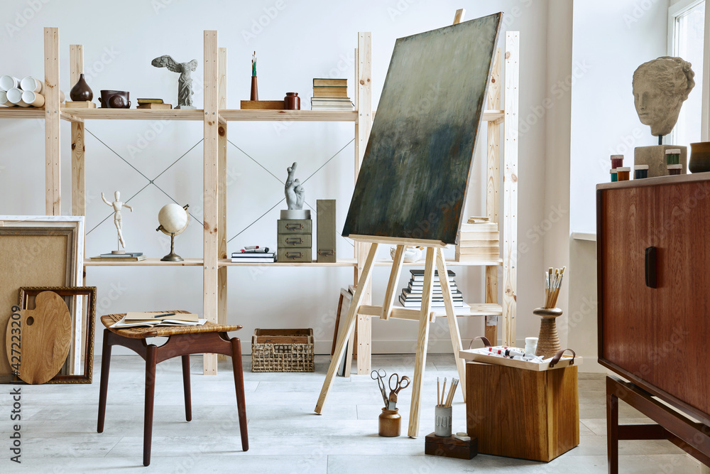Unique artist workspace interior with stylish teak commode, wooden easel, bookcase, artworks, painting accessories, decoration and elegant personal stuff. Modern work room for artist. Template. Unique artist workspace interior with stylish teak commode, wooden easel, bookcase, artworks, painting accessories, decoration and elegant personal stuff. Modern work room for artist. Template.