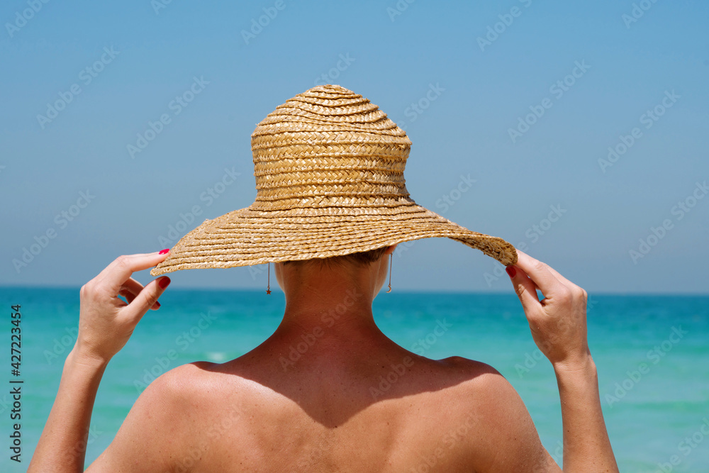 View from behind woman at the beach wearing straw hat against the sea