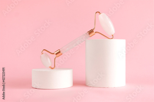 Rose quartz roller for facial massage on a concrete podium. Beauty and home skin care concept. Anti-aging therapy and lifting.