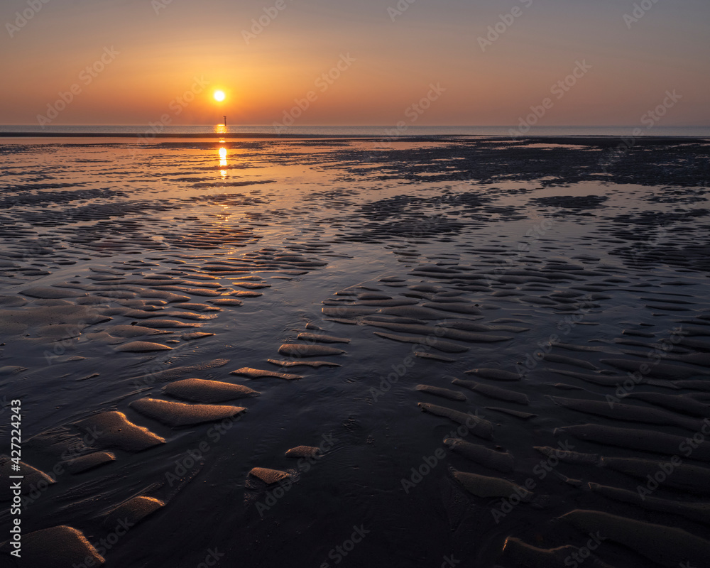 pattern in sand and colorful reflection of setting sun in water