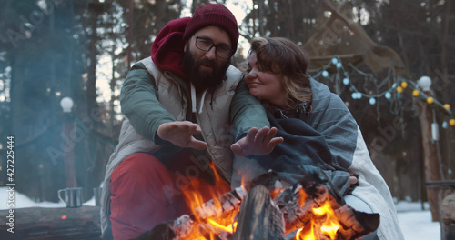 Man with woman sitting near campfire in winter forest