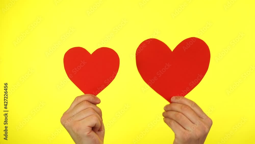 Male blogger hold in hands two little red hearts on a yellow background.