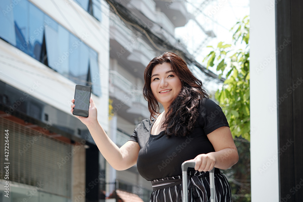 Beautiful smiling young woman with smartphone in hand waiting for taxi car to airport Beautiful smiling young woman with smartphone in hand waiting for taxi car to airport