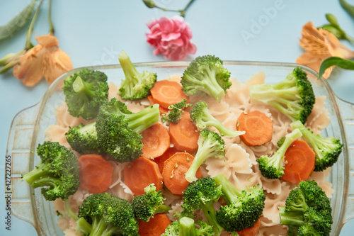 Proper nutrition: broccoli, carrots and pasta on blue background for baking.