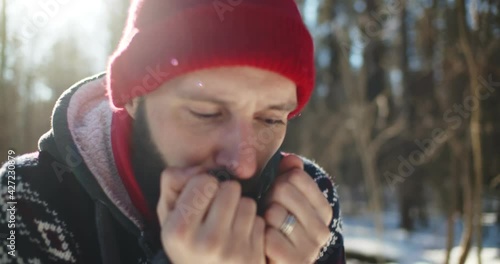 Young man hiker got lost in winter forest and blowing at frozen hands trying to get warm