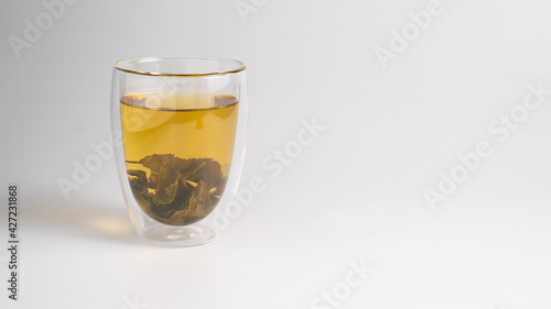 Green tea leaves are brewed in a glass mug. The concept of healthy herbal tea. Background with a cup of tea and copy