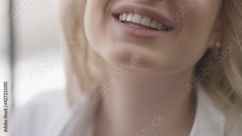 Close-up toothy smile of young slim charming Caucasian blond woman. Unrecognizable positive millennial smiling having fun indoors. Happiness and joy concept