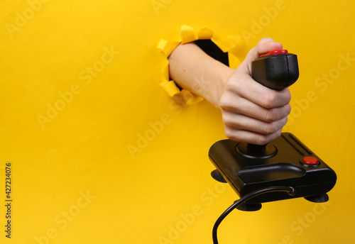 Bild auf Leinwand Female hand holds retro joystick through torn hole yellow paper