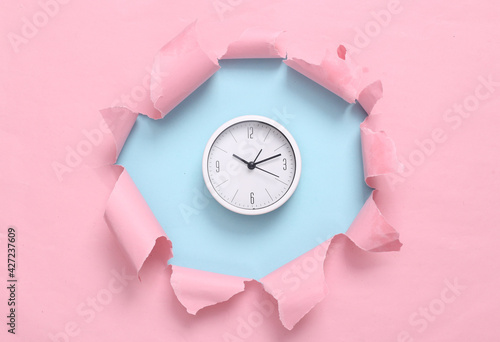 Clock through torn hole on blue-pink pastel background. Business concept. Pastel color trend. Minimalism