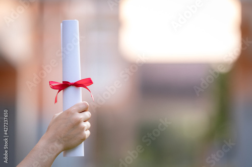 Close-up shot of a university graduate holding a degree certification to shows and celebrate education success on the college commencement day. Education stock photo