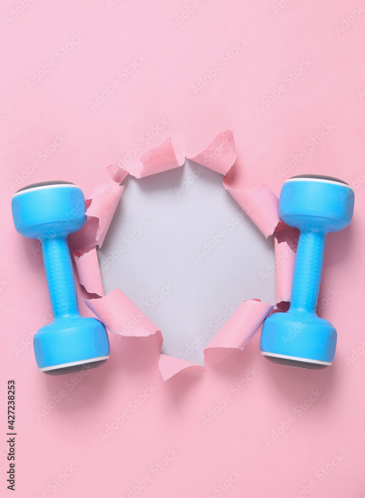 Dumbbells on pink background with ripped hole for copy space Dumbbells on pink background with ripped hole for copy space