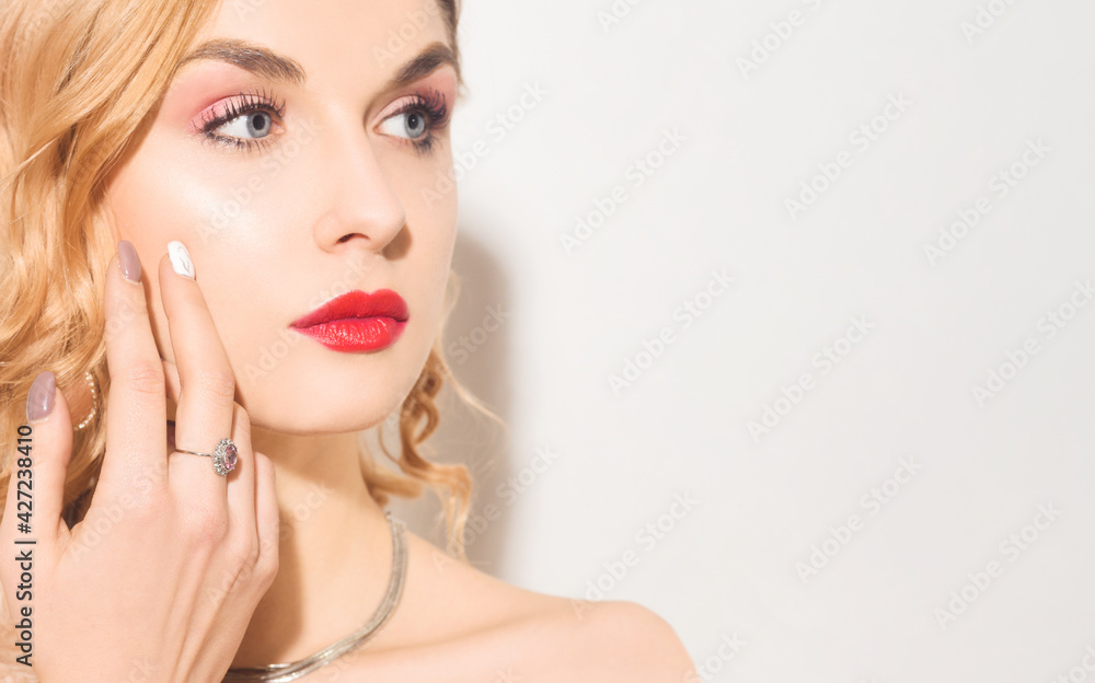 Blonde in silver and diamonds, obesity, earrings, rings. Woman with beautiful long nails and manicure. Girl with beautiful makeup, red lips on a white background, portrait. Place for text Blonde in silver and diamonds, obesity, earrings, rings. Woman with beautiful long nails and manicure. Girl with beautiful makeup, red lips on a white background, portrait. Place for text
