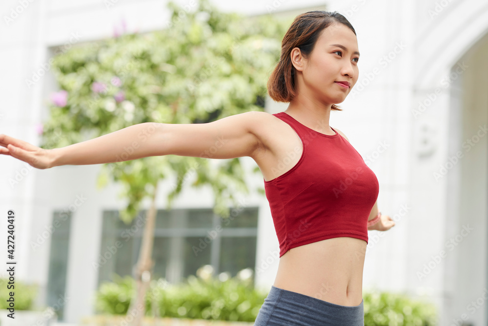 Pretty slim young Asian woman stretching and warming up before training utdoors