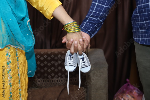 Close up picture of happy couple of pregnant mother with father holding hands small shoes. Indian couple hands holding baby boys shoes