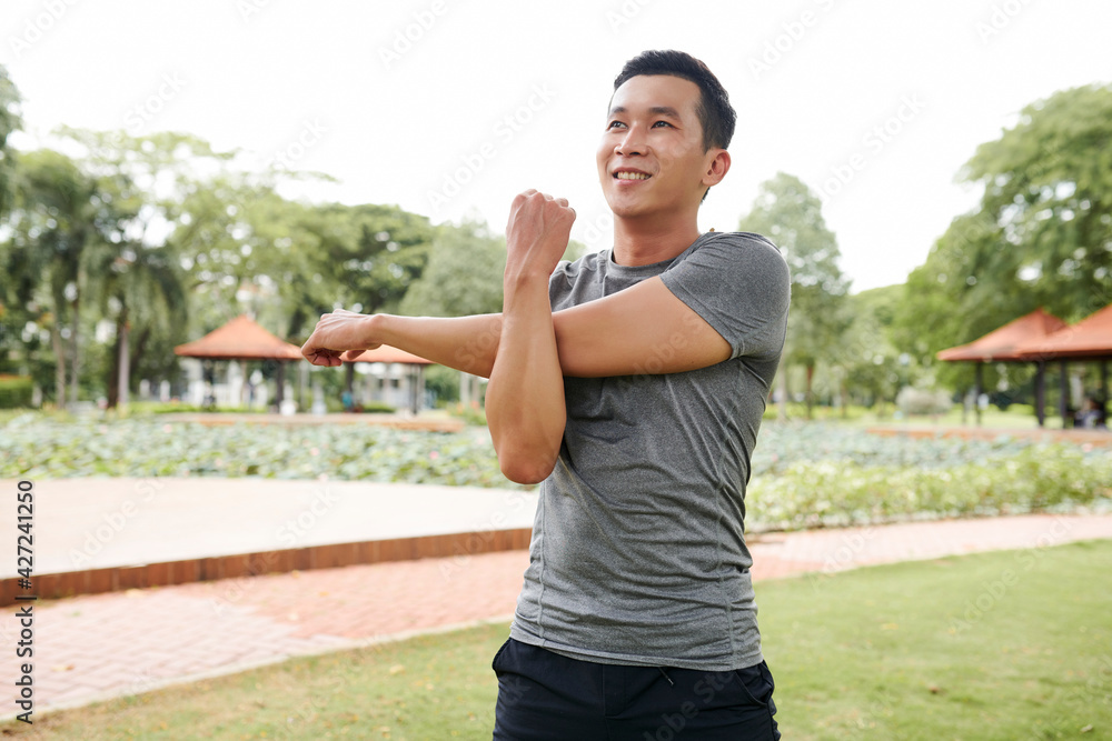 Portrait of handsome fit young Asian man stretching arms and warming up after jogging outdoors Portrait of handsome fit young Asian man stretching arms and warming up after jogging outdoors