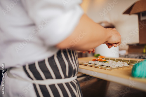 Close up shot of a professional sushi chef preparing salmon maki roll in a restaurant. Traditional Japanese omakase style. Concept of hospitality.