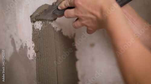 A male tiler manually glues ceramic tiles to the bathroom wall. Aligning the adhesive on the wall for gluing the tiles. The builder attaches the tiles to the wall with cement.
