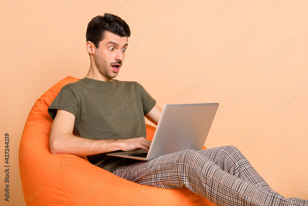 Photo portrait of man in chair working on laptop doing project amazed browsing internet isolated on pastel beige color background Photo portrait of man in chair working on laptop doing project amazed browsing internet isolated on pastel beige color background