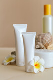 Natural beauty cosmetic tube mockup product for skincare with sea shell tropical plumeria flowers on stone pedestal beige background. Natural body care sun protect cream cosmetic tube