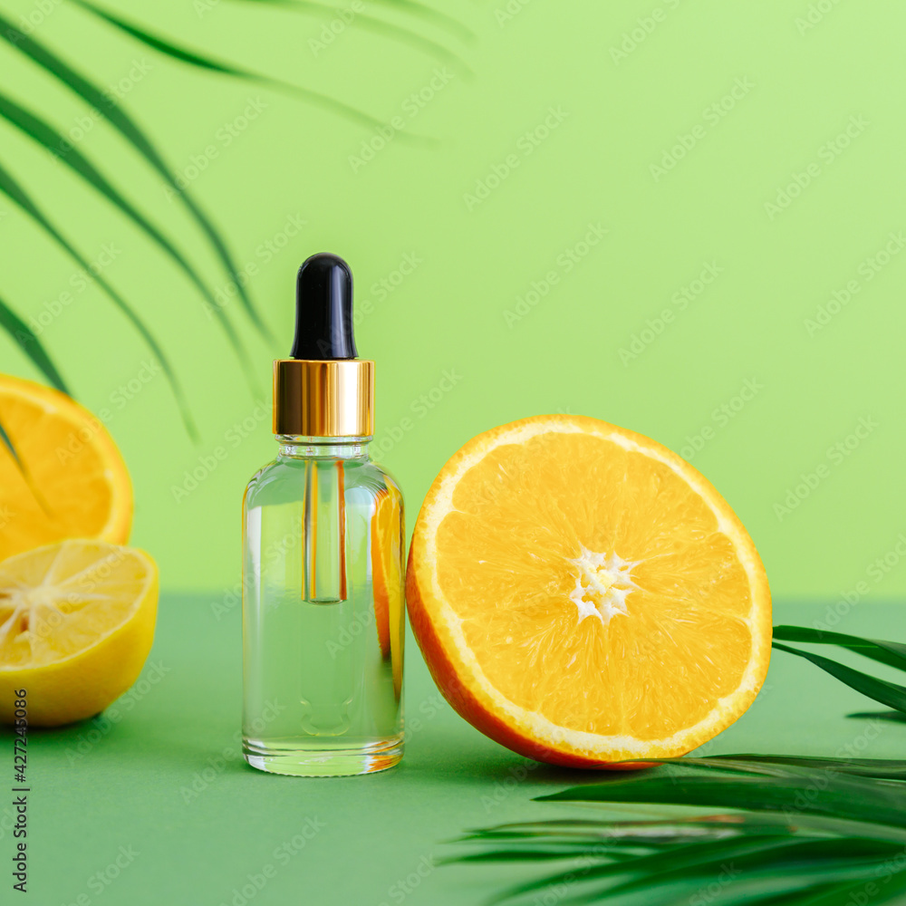 Cosmetic serum Vitamin C in glass bottle with pipette dropper. Orange essential oil with citrus ingredients Vitamin C palm leaves on color green background. Natural skin care Face Cosmetics. Square Cosmetic serum Vitamin C in glass bottle with pipette dropper. Orange essential oil with citrus ingredients Vitamin C palm leaves on color green background. Natural skin care Face Cosmetics. Square