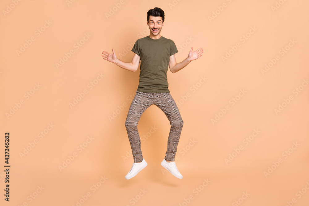 Full length body size photo of jumping funny man smiling wearing casual clothes isolated on pastel beige color background