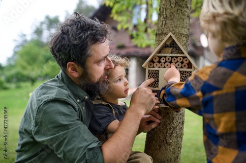 Small children with father holding bug and insect hotel in garden, sustainable lifestyle. © Halfpoint