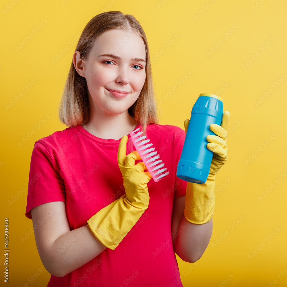 Young blonde happy smiling woman ready to cleaning house with household supplies isolated over yellow color background. Woman Portrait with cleaning brush cleaner in rubber gloves. Closeup Square Young blonde happy smiling woman ready to cleaning house with household supplies isolated over yellow color background. Woman Portrait with cleaning brush cleaner in rubber gloves. Closeup Square