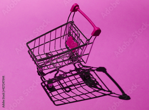 Shopping trolley on pink background with shadows. Mini shopping concept