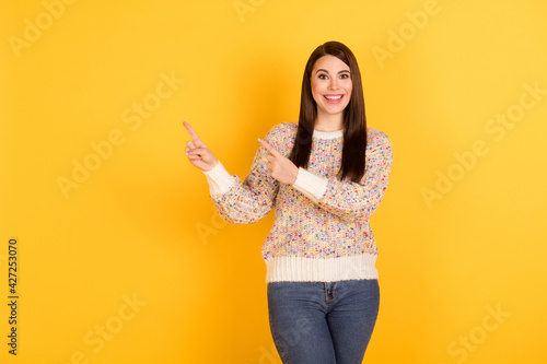 Photo portrait of amazed brunette showing empty space smiling overjoyed isolated on vivid yellow color background