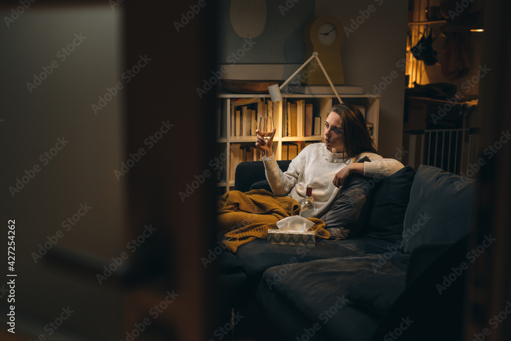depressed woman sitting on sofa and drinking alcohol. evening scene