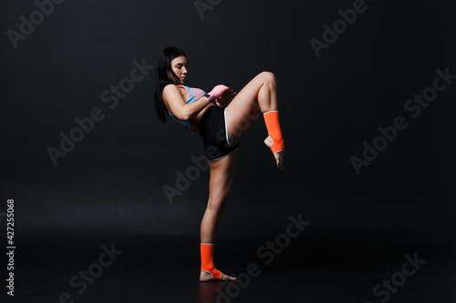 Sportsman muay thai woman boxer posing in training studio at black background.