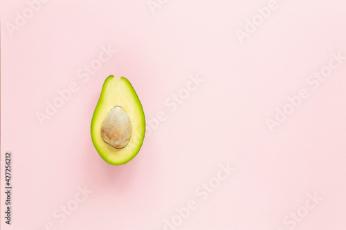A half of avocado with seed on pink background. Top view.
