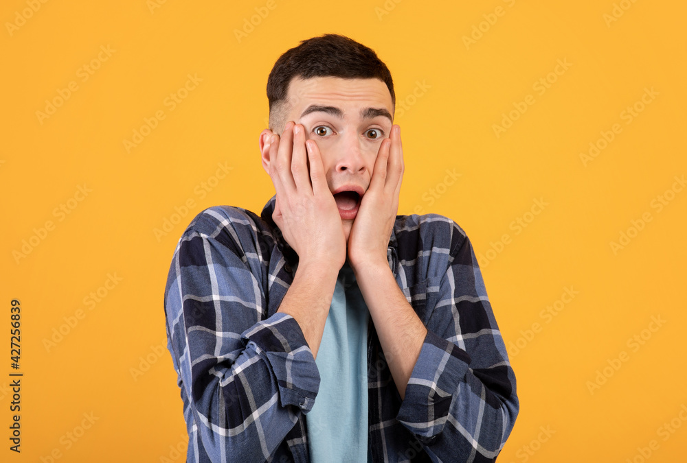 Young hipster man feeling afraid, trying to hide his face on orange studio background Young hipster man feeling afraid, trying to hide his face on orange studio background