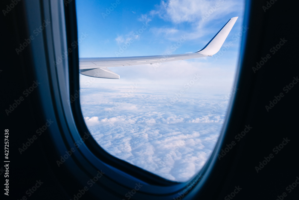 An airplane wing looks out the airplane window with a clear sky and beautiful clouds with sunbeams