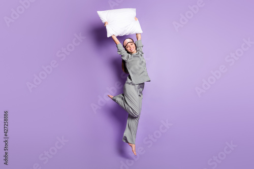 Full length body size photo of girl jumping with white pillow on pajama party isolated pastel violet color background