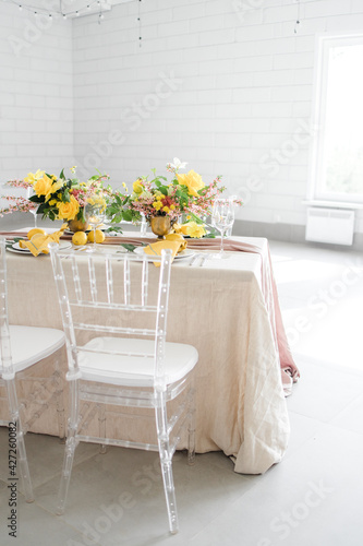serving on a lemon-colored table. Transparent chairs, rectangular table in a white hall © Anna