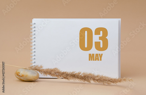 may 03. 03th day of the month, calendar date. White blank sheet of notepad, stones, dry sprig of grass, on beige background.Spring month, day of the year concept photo