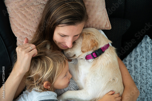 Young mother cuddling with her toddler daughter and their cute dog